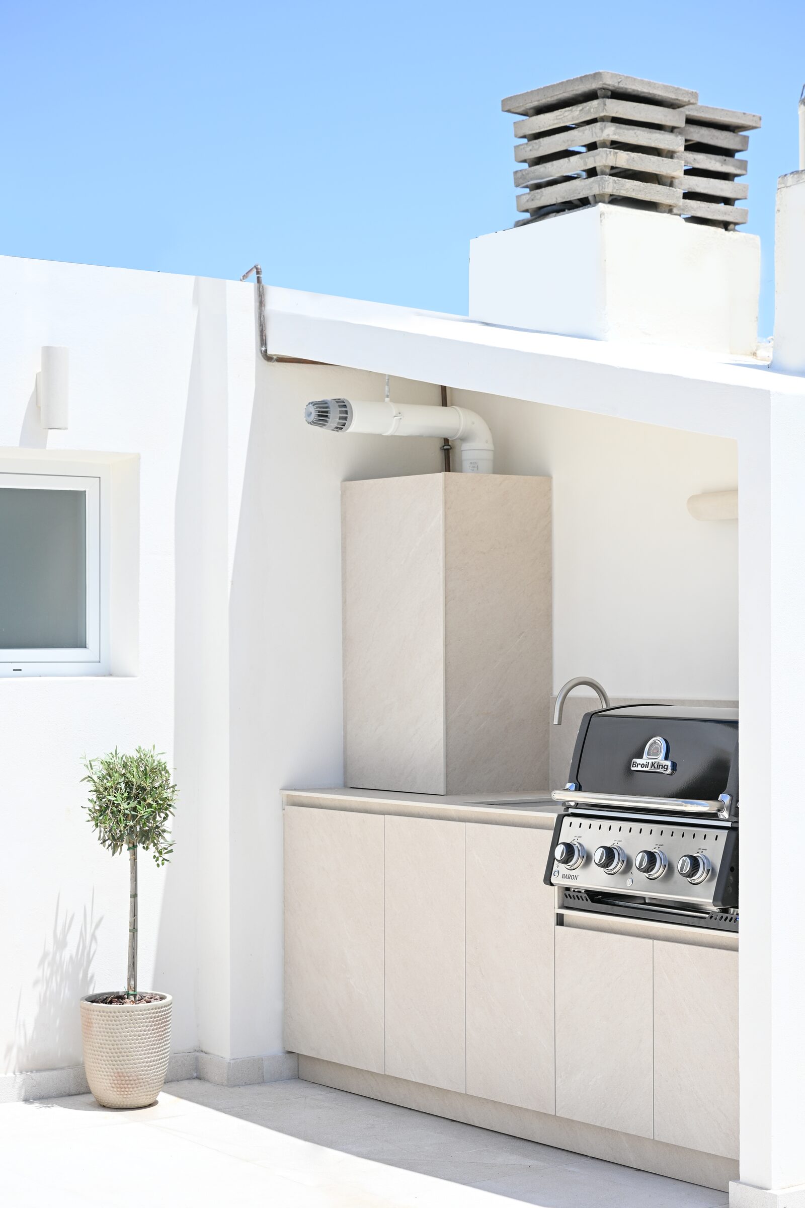Rooftop terrace with parasol, outdoor grill and chimney stacks against a deep blue sky.