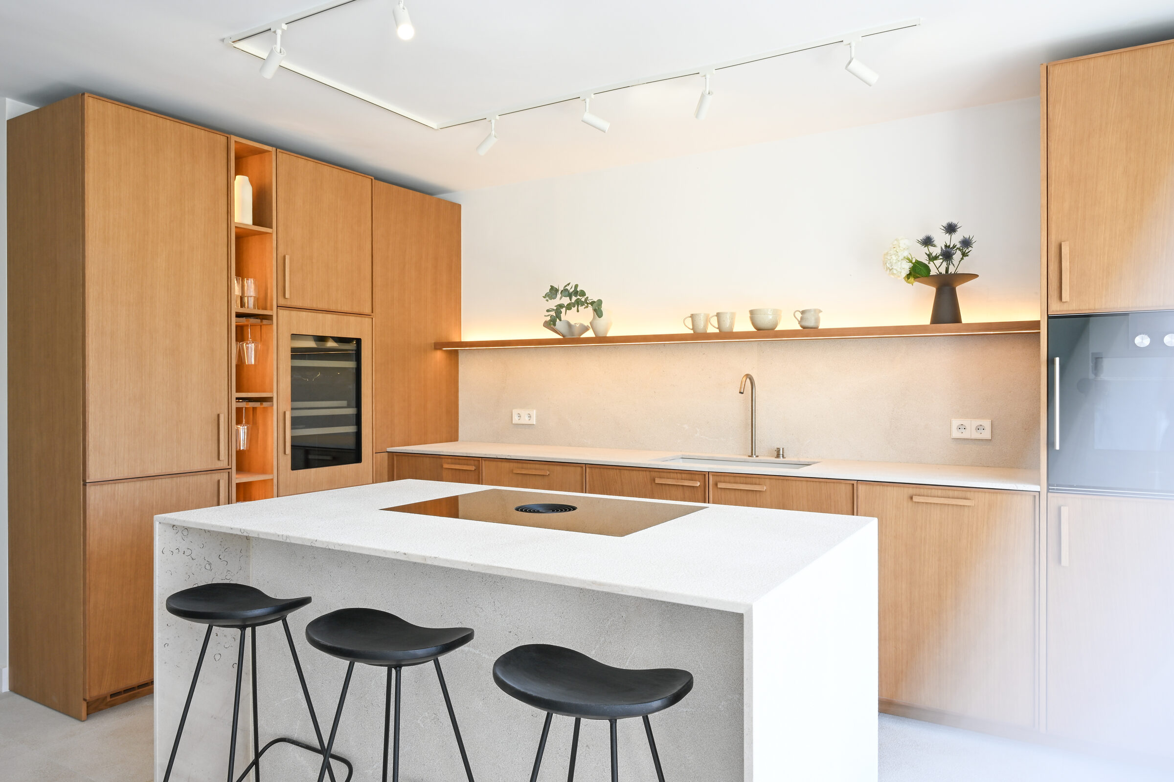 Wide angle of the oak kitchen showing the full island, three black stools, pantry wall and glass door to the terrace.