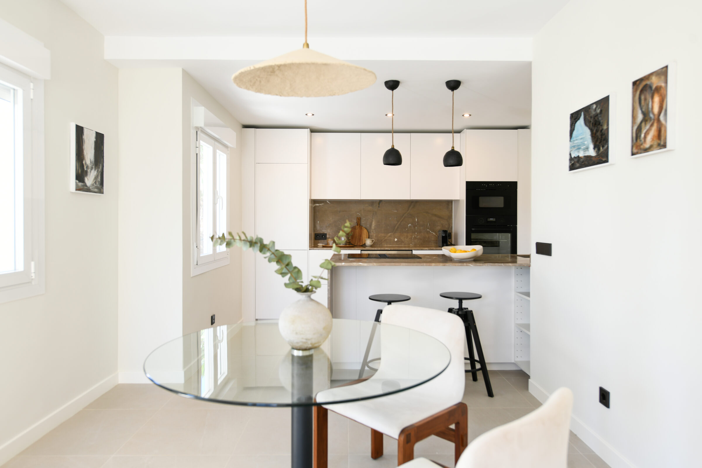 Round glass dining table beside the open kitchen, full of natural light.