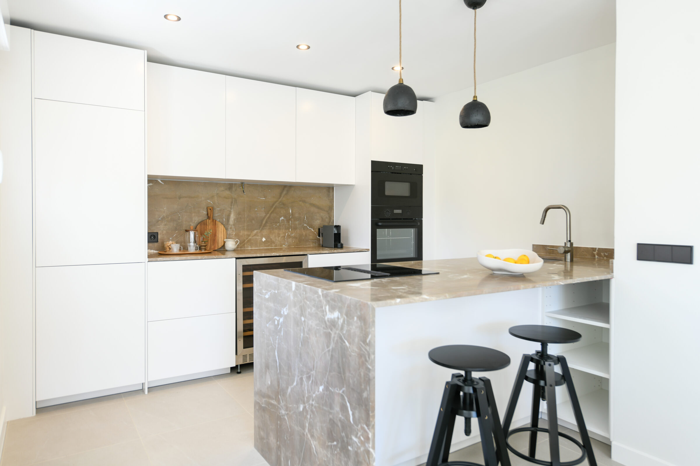 White kitchen with a marble island and warm walnut backsplash in the Islandia home.