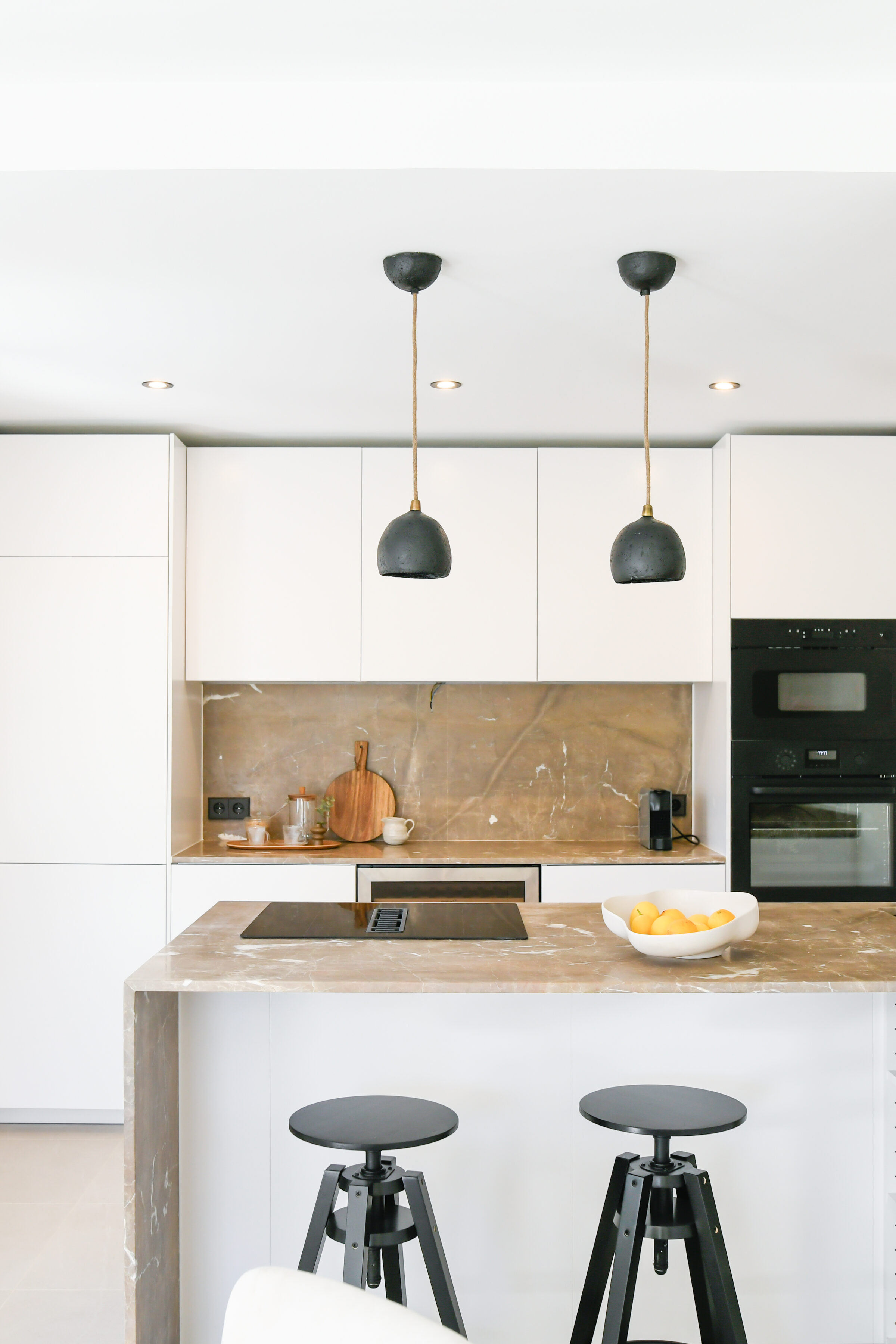Marble kitchen island with black ceramic pendant lights and a walnut backsplash.