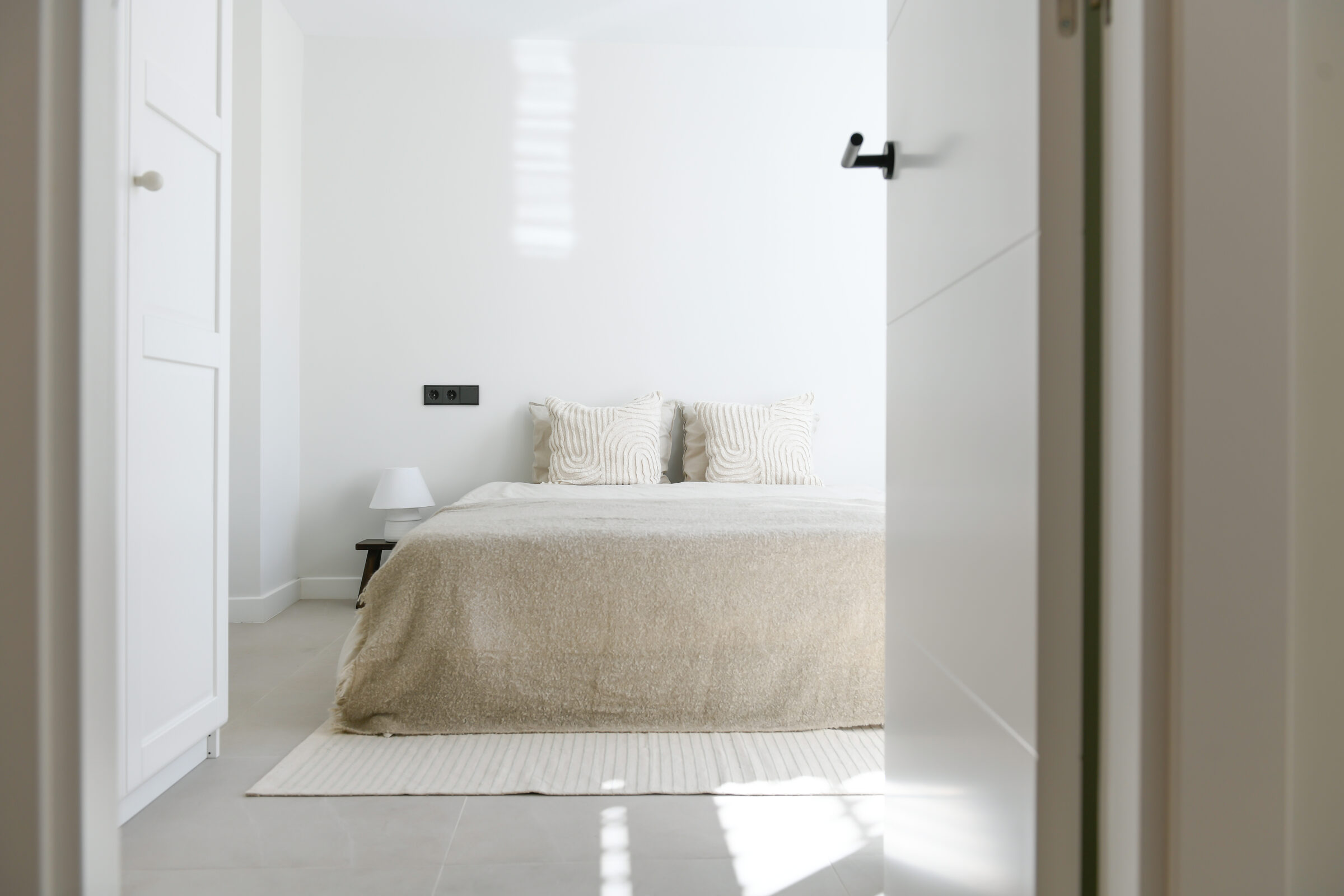 Master bedroom in soft beige and linen tones, framed by a doorway.