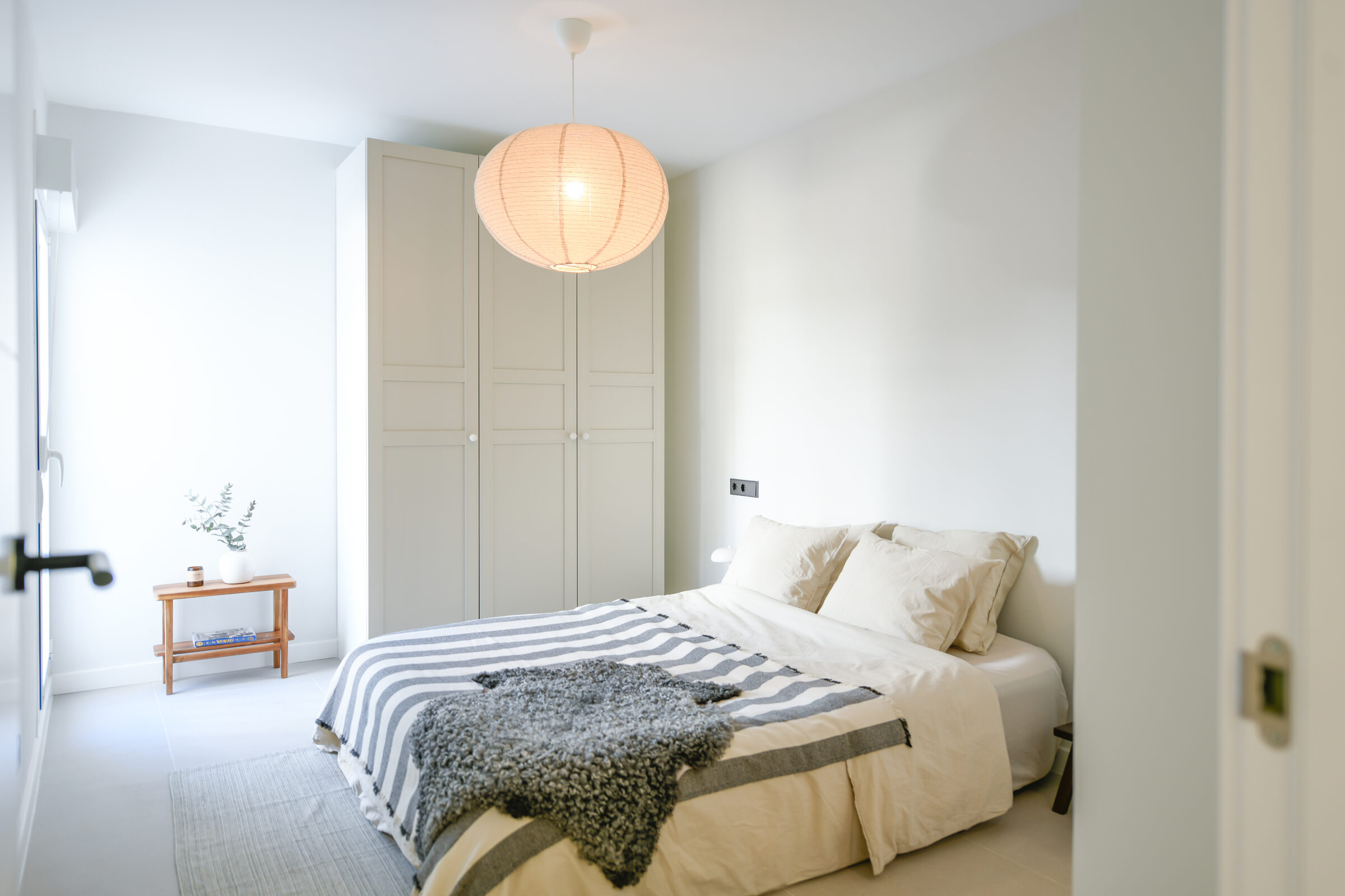 Second bedroom with a paper-globe pendant, built-in wardrobe and striped throw.