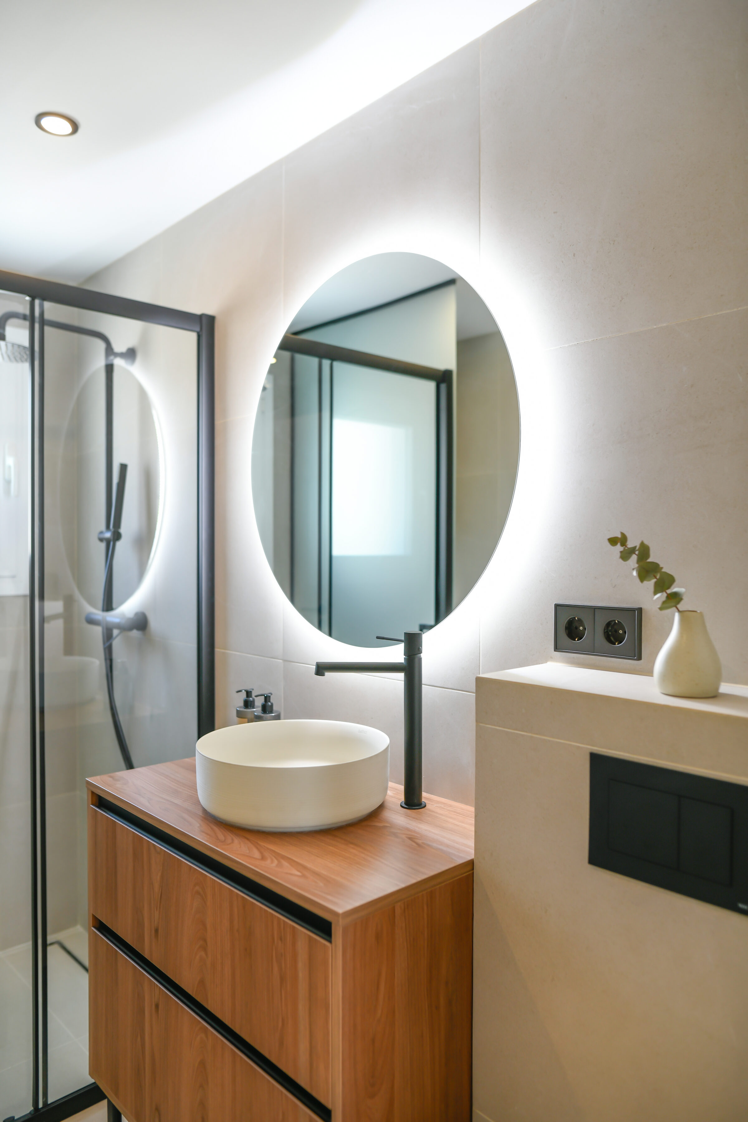 Main bathroom with a backlit round mirror, walnut vanity and walk-in shower.