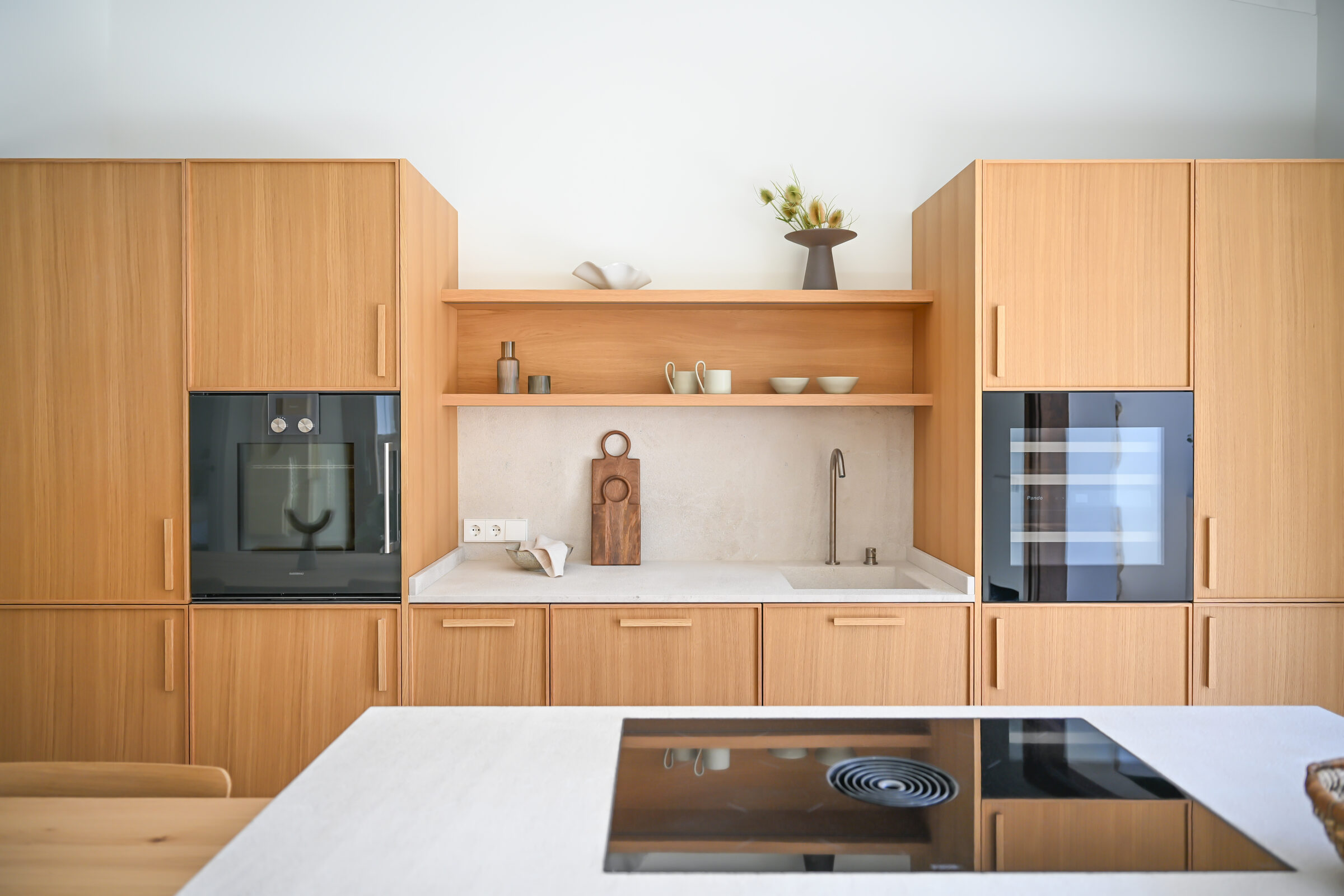 Full walnut kitchen elevation with open shelving, stone backsplash and built-in oven.