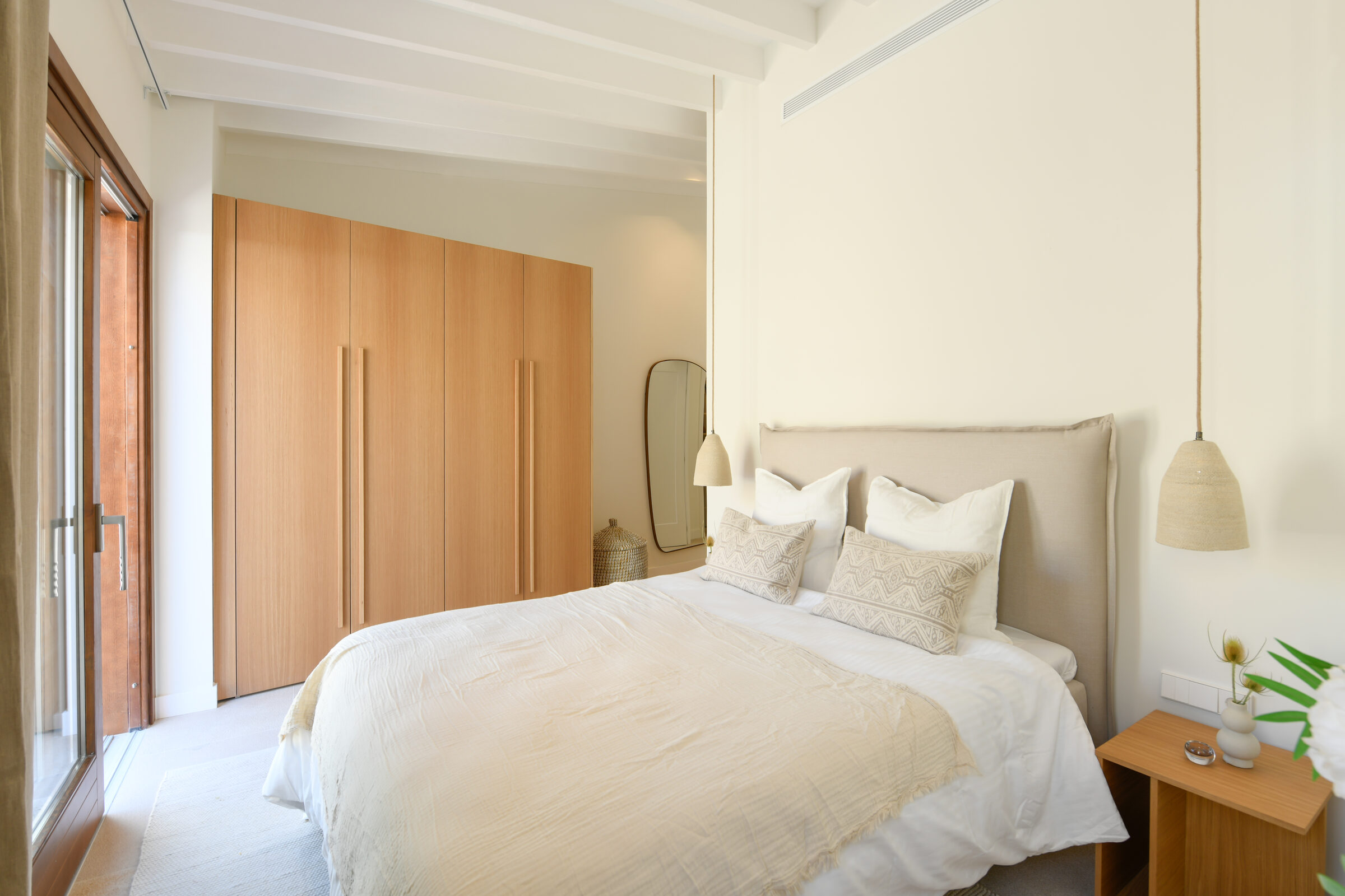 Master bedroom with full-height walnut wardrobes and a sculptural mirror.