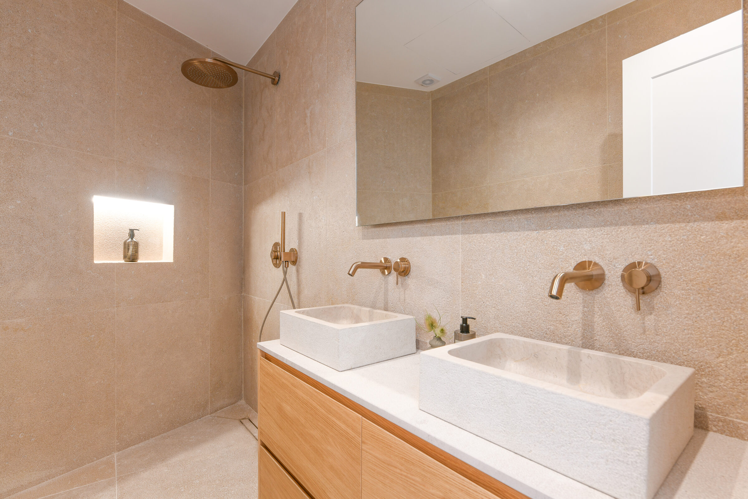 Stone-lined bathroom with double vessel basins, brushed-brass fittings and rain shower.