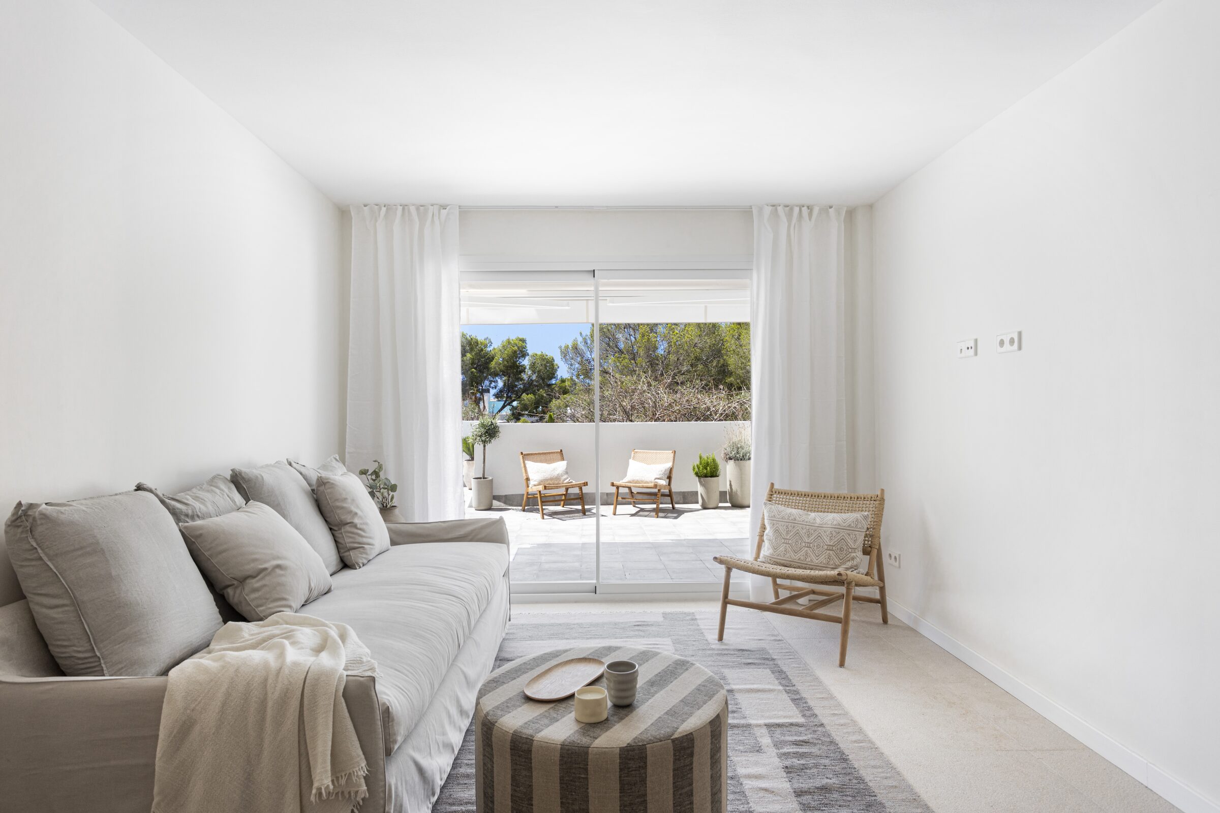 Linen sofa and woven armchair in the living room, opening through full-height glass to the terrace.