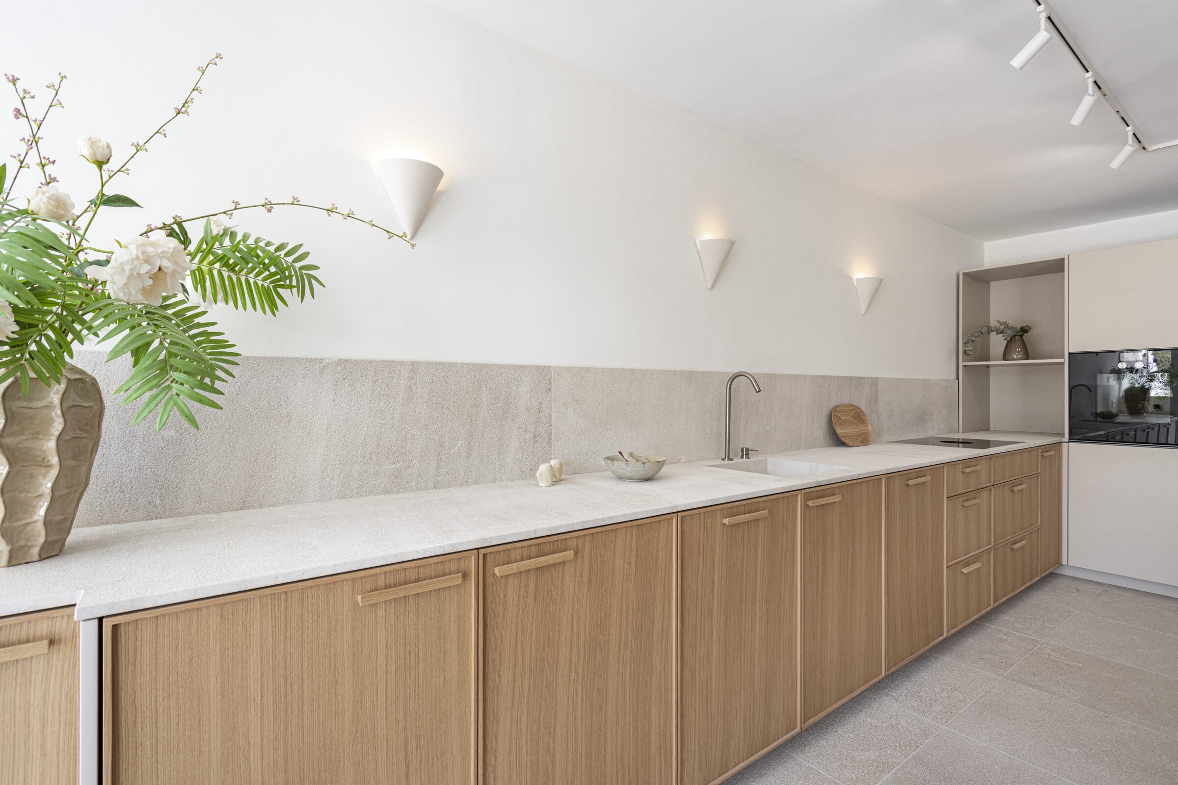 Walnut kitchen elevation in soft afternoon light with a hand-thrown vase of jasmine on the marble counter.