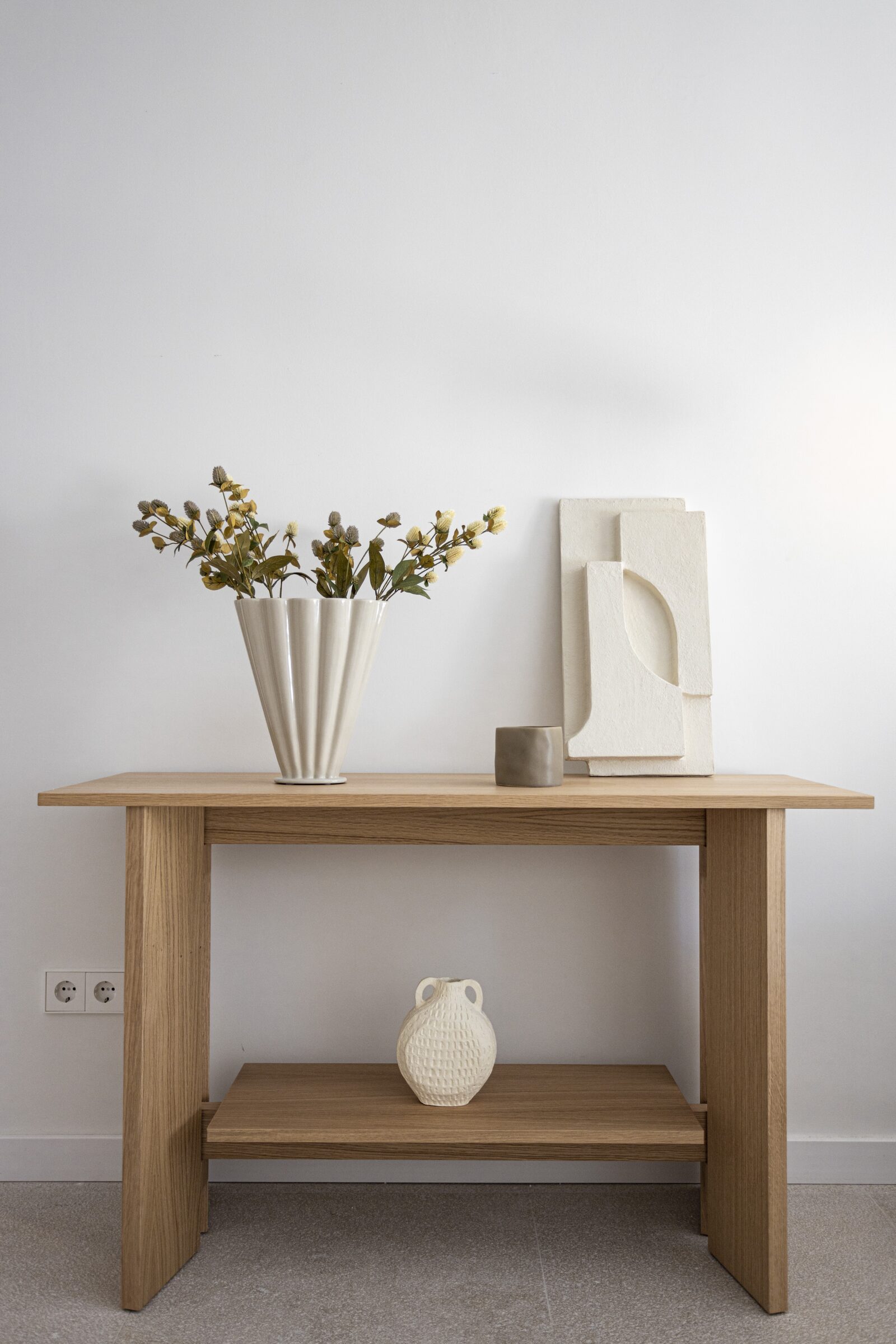 Oak entry console styled with a fluted ceramic vase, dried wildflowers and a sculptural relief.