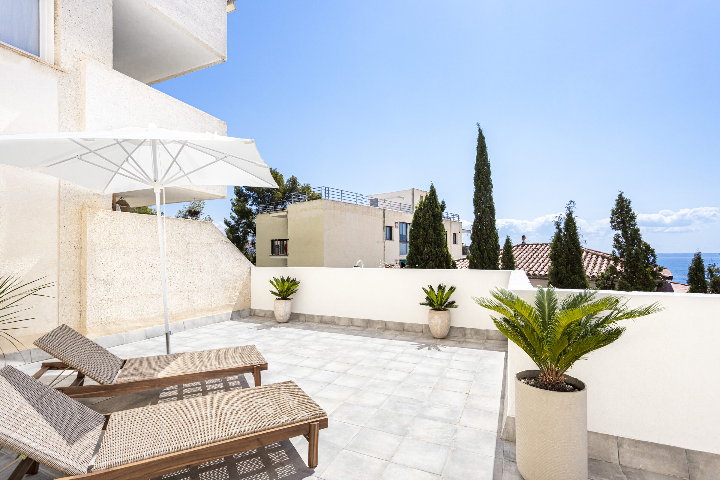 Wicker sun loungers under a parasol on the bright stone terrace.
