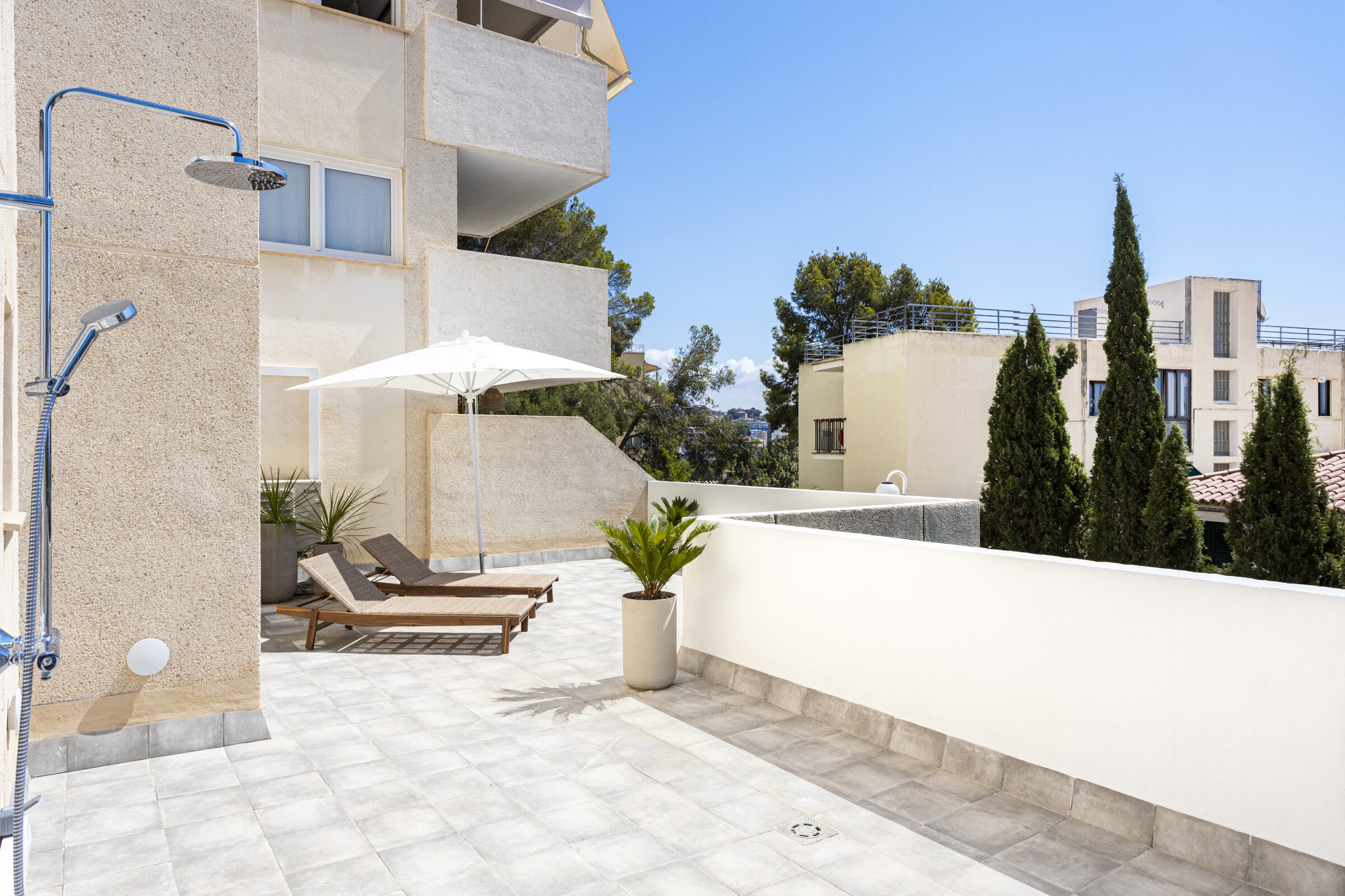 Outdoor shower zone with cypress trees, sun loungers and white parasol on the side terrace.