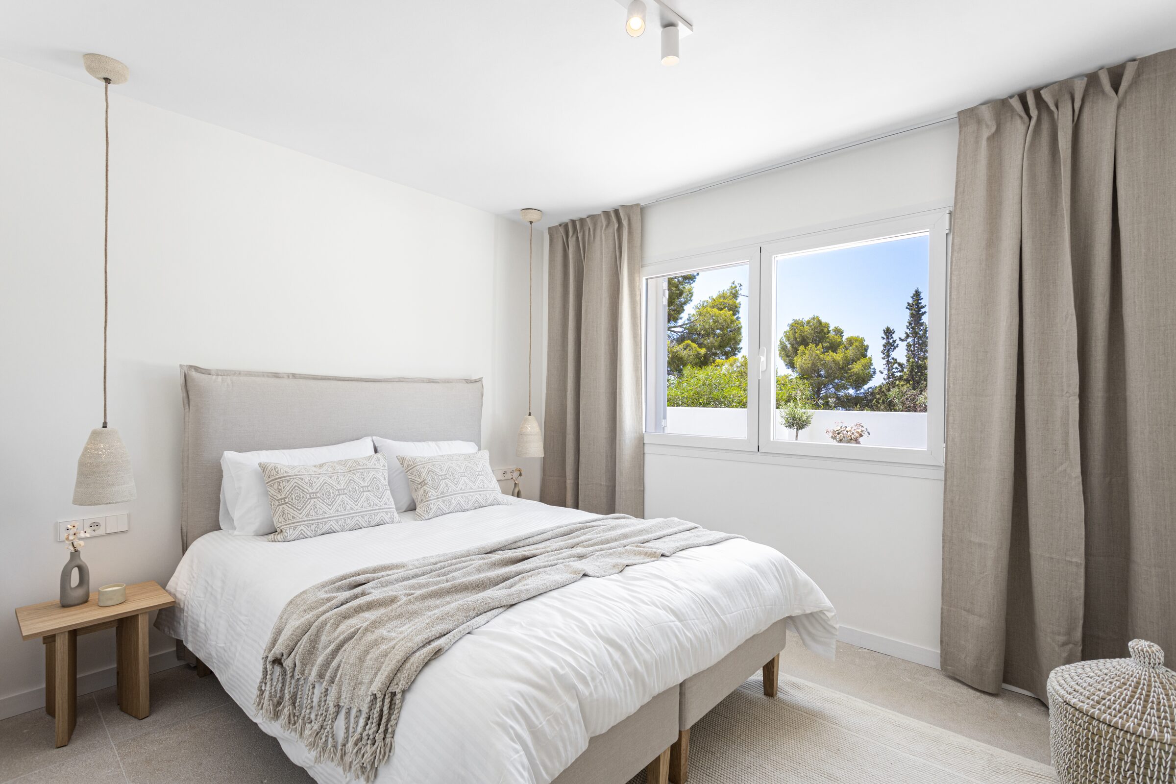 Master bedroom with linen-upholstered headboard and a window framing the morning light over the bay.