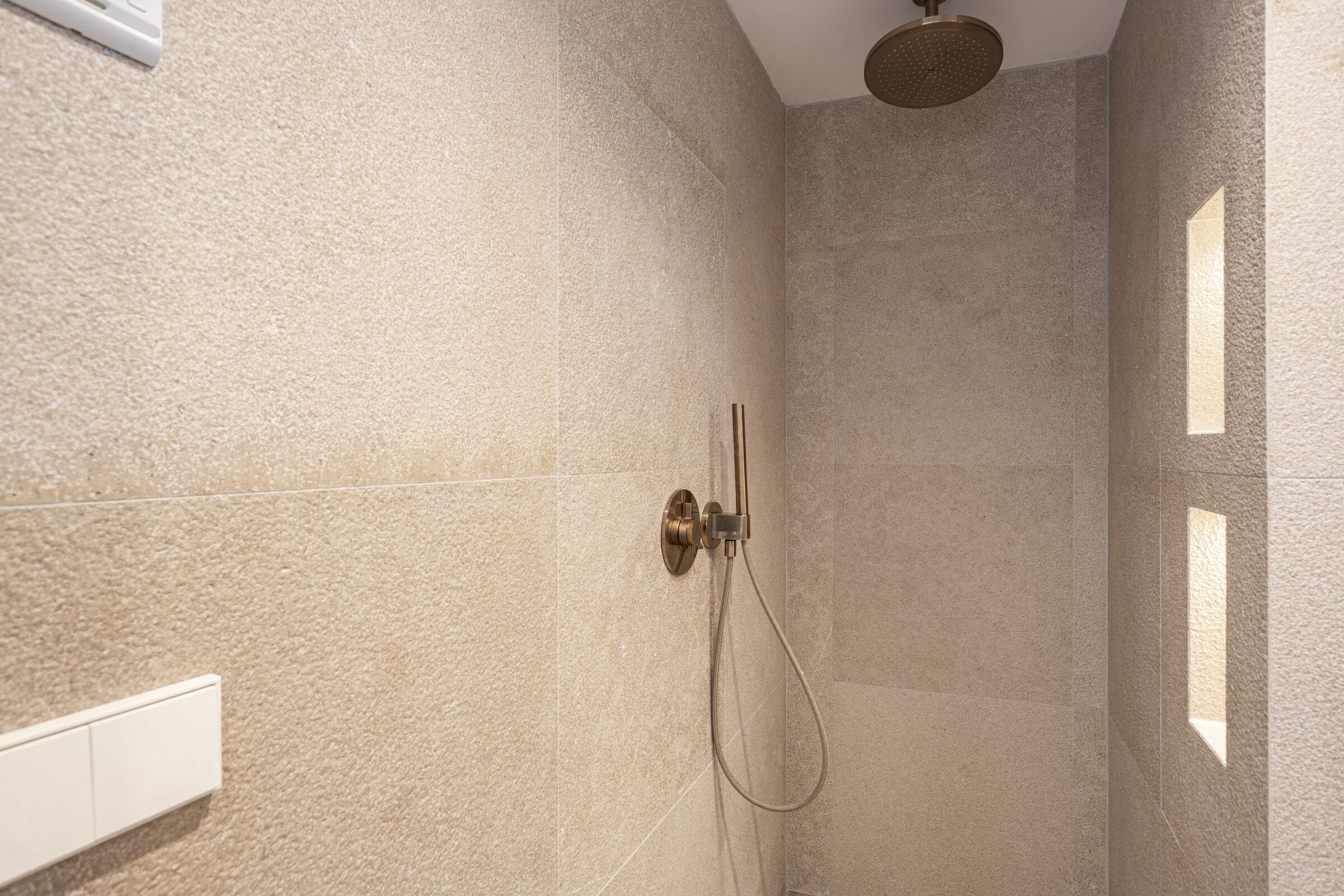 Stone-clad bathroom with rain shower and brushed-bronze Hansgrohe fittings.